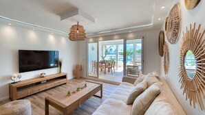 A modern living room with a flat-screen TV, wooden coffee table, and a beige sofa. - Six View - Beach Front Apartment (saint martin)
