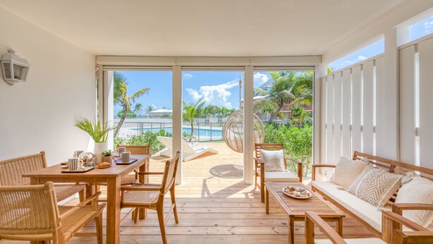 A wooden deck with outdoor furniture, including a table, chairs, and a sofa. - Six View - Beach Front Apartment (saint martin)