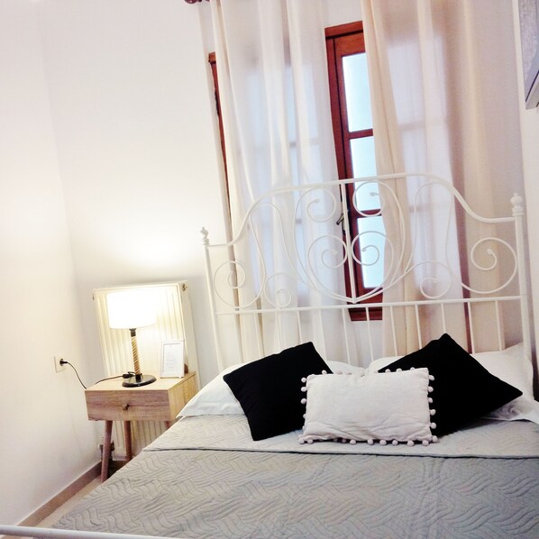 A neatly made bed with a white headboard, a bedside table with a lamp, and a window with curtains.