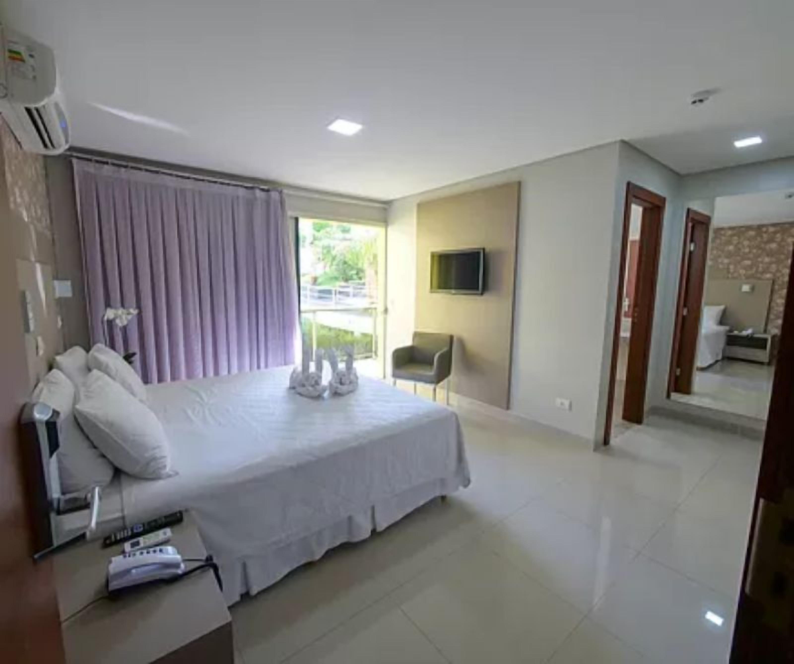 Una habitación de hotel con una cama grande, un televisor en la pared y una silla.