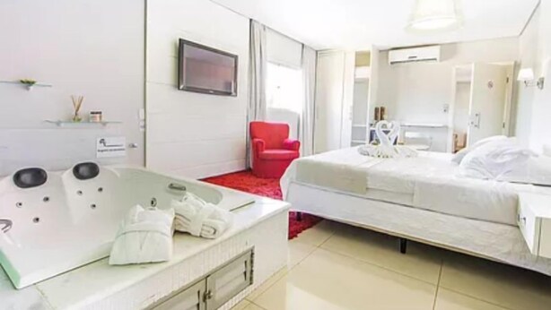 Habitación de hotel moderna con una bañera grande, una cama individual, una silla roja y un televisor.
