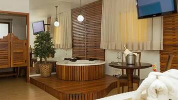 A modern hotel room with a wooden floor, a round hot tub, a television, and a large mirror.