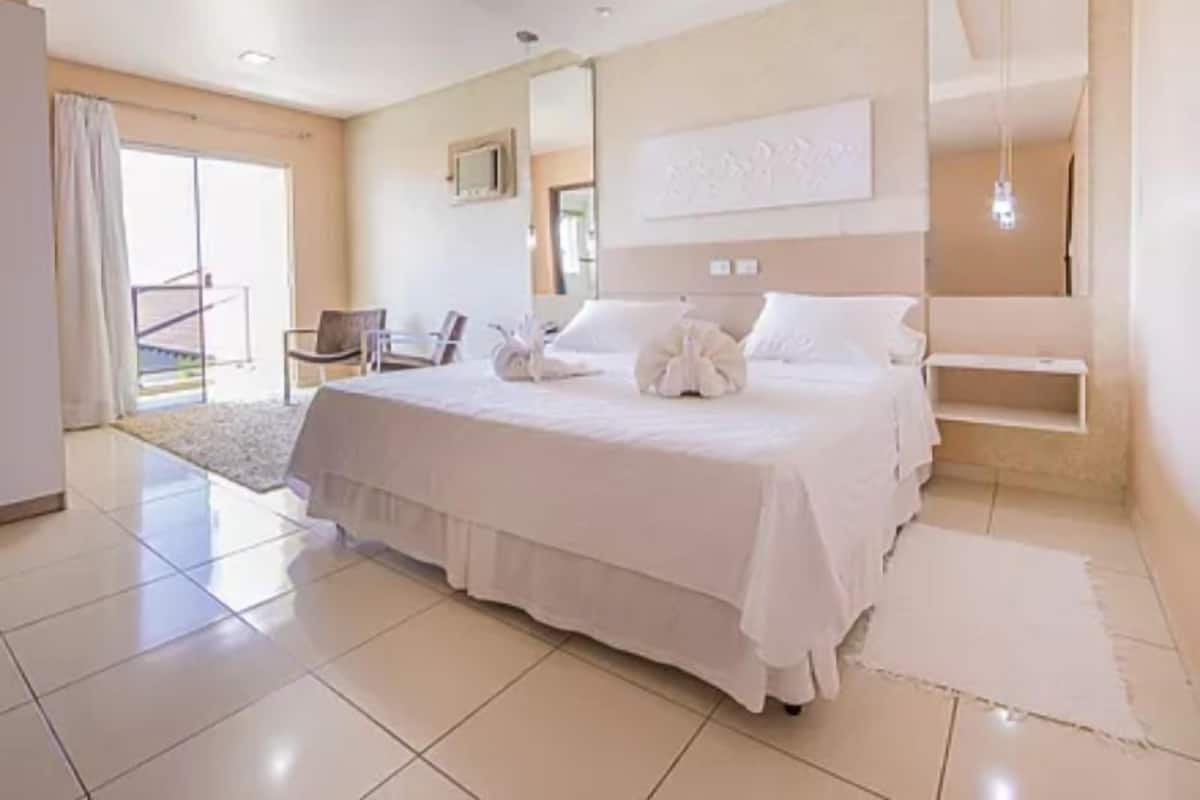 A modern bedroom with a large bed, a mirror, and a sliding glass door leading to a balcony.