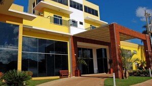 Un edificio moderno con grandes ventanales, fachada amarilla y zona de entrada de ladrillo.