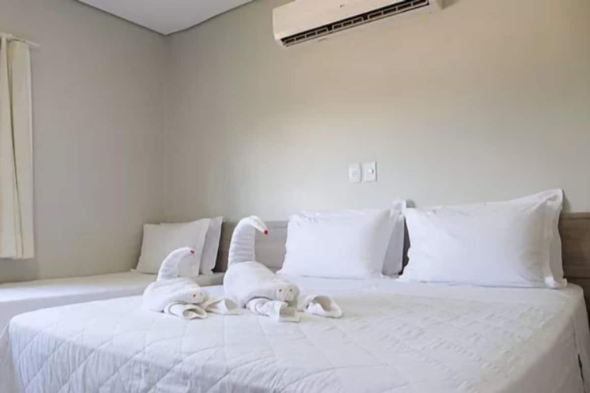 A hotel room with two beds, a large window with curtains, and an air conditioning unit on the wall.