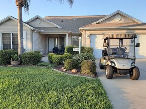 A residential house with a garage, a golf cart, and well-maintained landscaping. - Amazing Home Centrally Located! Golf Cart Included & FREE WiFi! (The Villages)