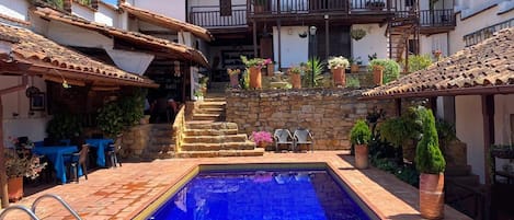 A pool area with a clear blue pool, stone steps leading up to a house, and outdoor seating.