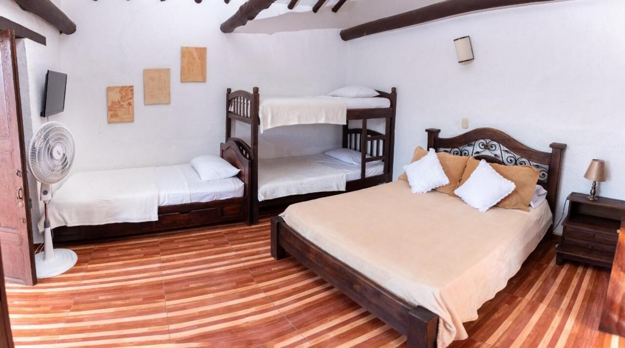A room with a large bed, two smaller beds, a fan, and a wooden floor.