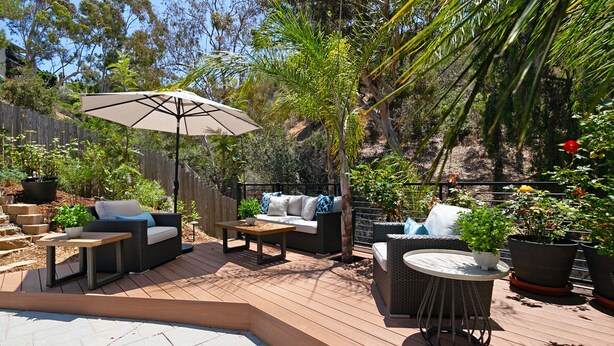 Une terrasse avec des meubles d’extérieur, notamment des canapés et une table, entourée de plantes en pot et dotée d’une plateforme en bois.