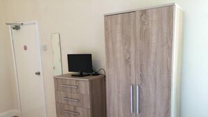Una habitación con un armario de madera, un mueble pequeño con cajones y una puerta con letrero de prohibido fumar.