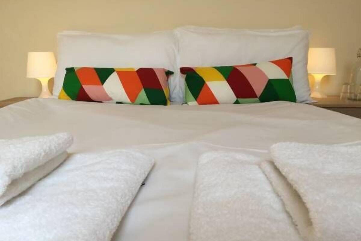 A neatly made bed with white linens and colorful geometric pillows.