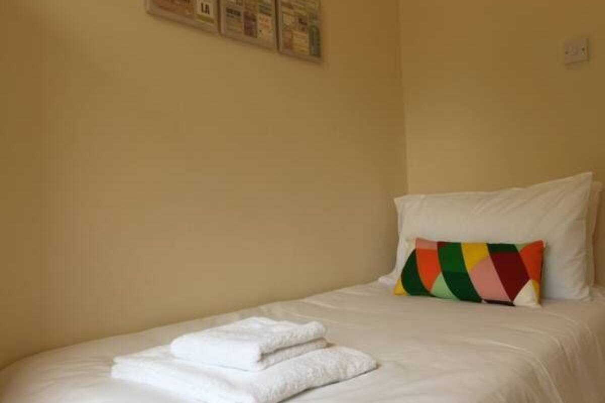 A neatly made bed with white linens and a colorful pillow.