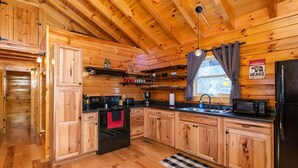 A wooden cabin interior with a kitchen featuring wooden cabinets, a stove, a sink, and a refrigerator.