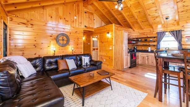 A cozy log cabin interior with a leather sofa, wooden dining table, and a kitchen area.