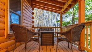 A wooden cabin with a covered porch, two wicker chairs, and a table.