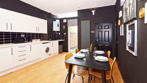 A modern kitchen with white cabinets, a black countertop, and a dining area with a black table and chairs. - Townhouse Plus @ 301 West Street Crewe (Crewe)