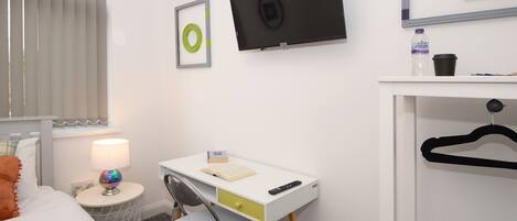 A bedroom with a bed, a desk with a chair, a TV, a window with blinds, and a water bottle on the nightstand.