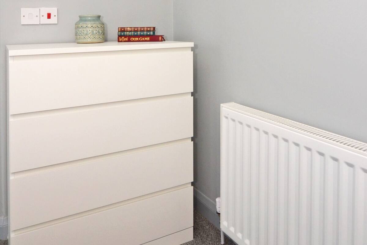 A room with a white dresser, a radiator, and three framed pictures on the wall.