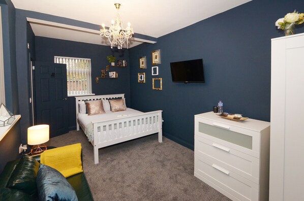 Une chambre à coucher avec un lit blanc, une commode, un téléviseur et un lustre.