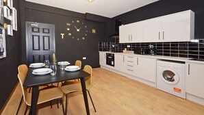 A modern kitchen with a black and white color scheme, a dining table set with plates and glasses, and a washing machine. - Townhouse Plus @ 301 West Street Crewe (Crewe)