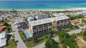 Une vue aérienne d’un hôtel avec une piscine, un parking et une plage en arrière-plan.