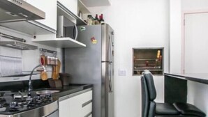 A compact kitchen with modern appliances, a dining area with a bar stool, and a small window. - Apartment next to the Grêmio Arena (Farrapos)
