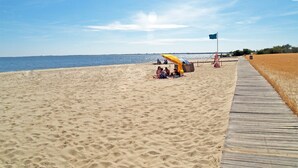 Una platja sorrenca amb un passeig marítim de fusta, un parasol groc i una bandera.