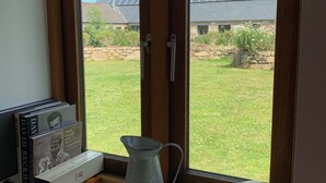A window with a view of a grassy yard and a building with solar panels. - Wonderful Wallow barn - Close  to Sennen Cove  & Porthcurno Cove & Coastal Path (Penzance)