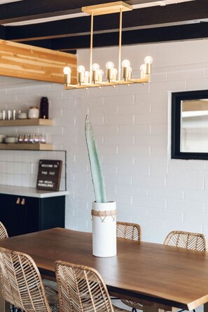 Un coin repas avec une table en bois, des chaises en osier, un vase blanc contenant une plante et un luminaire suspendu au design moderne.