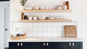Een keuken met witte bakstenen muren, houten planken en zwarte kastjes.