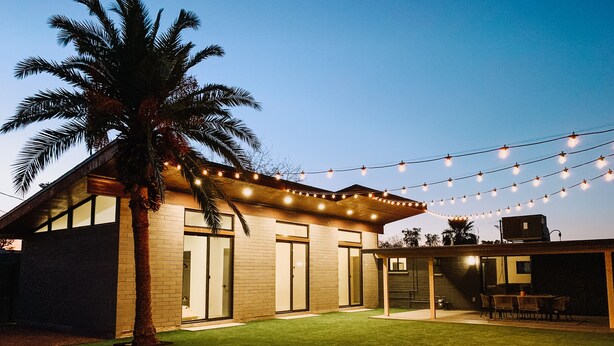 Een modern huis met een overdekt terras, een gazon en lichtjes.