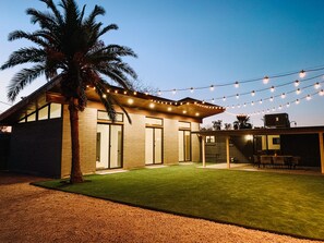 Une maison moderne dotée d’un patio couvert, d’une pelouse et de guirlandes lumineuses.