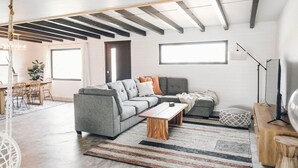 Een moderne woonkamer met een grijze modulaire bank, een houten salontafel en een gestreept vloerkleed.
