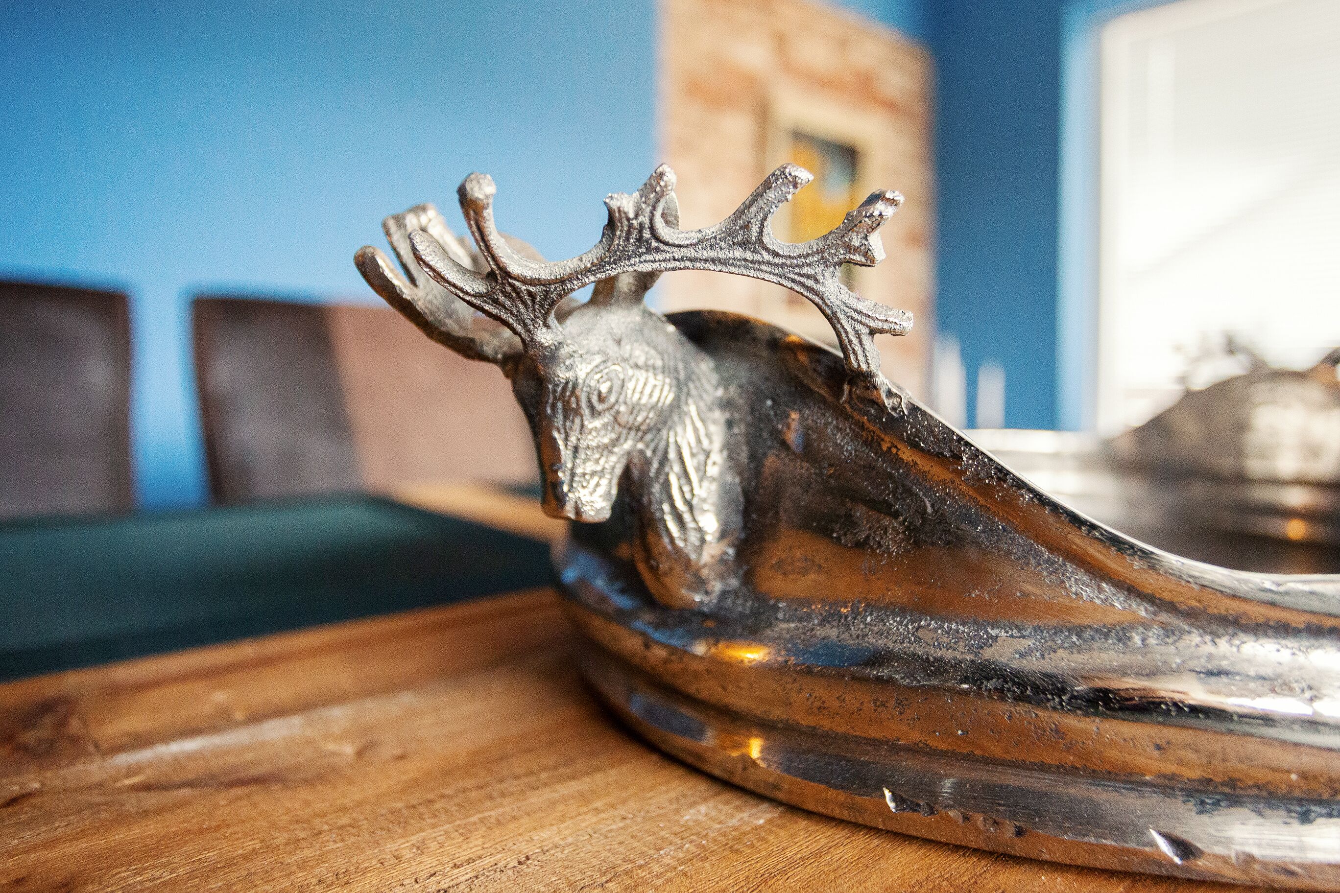 A silver decorative item with a carved deer head on a wooden surface.