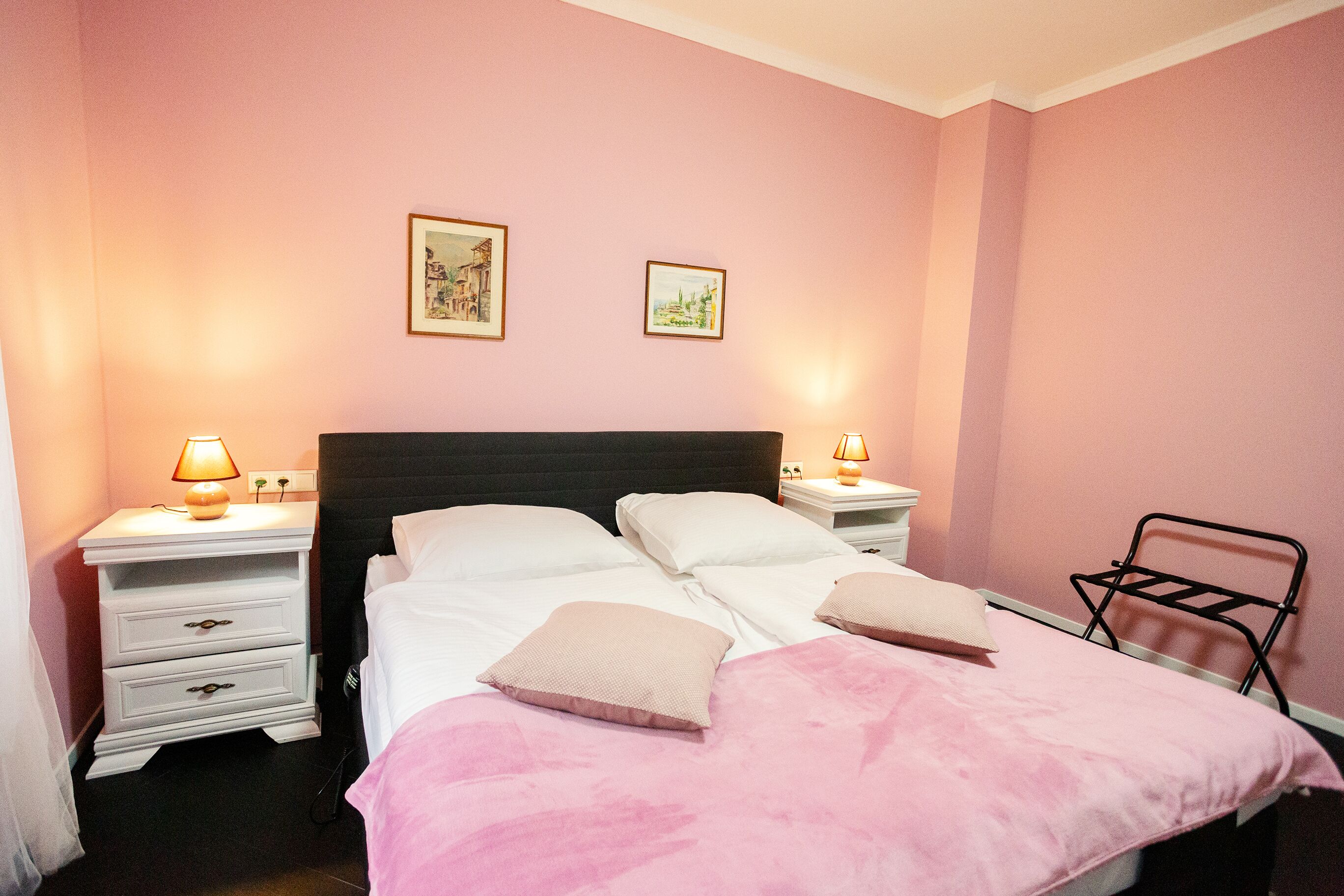 Ein Schlafzimmer mit einem Bett, zwei Nachttischen mit Lampen, einem Sessel und zwei gerahmten Bildern an der Wand.
