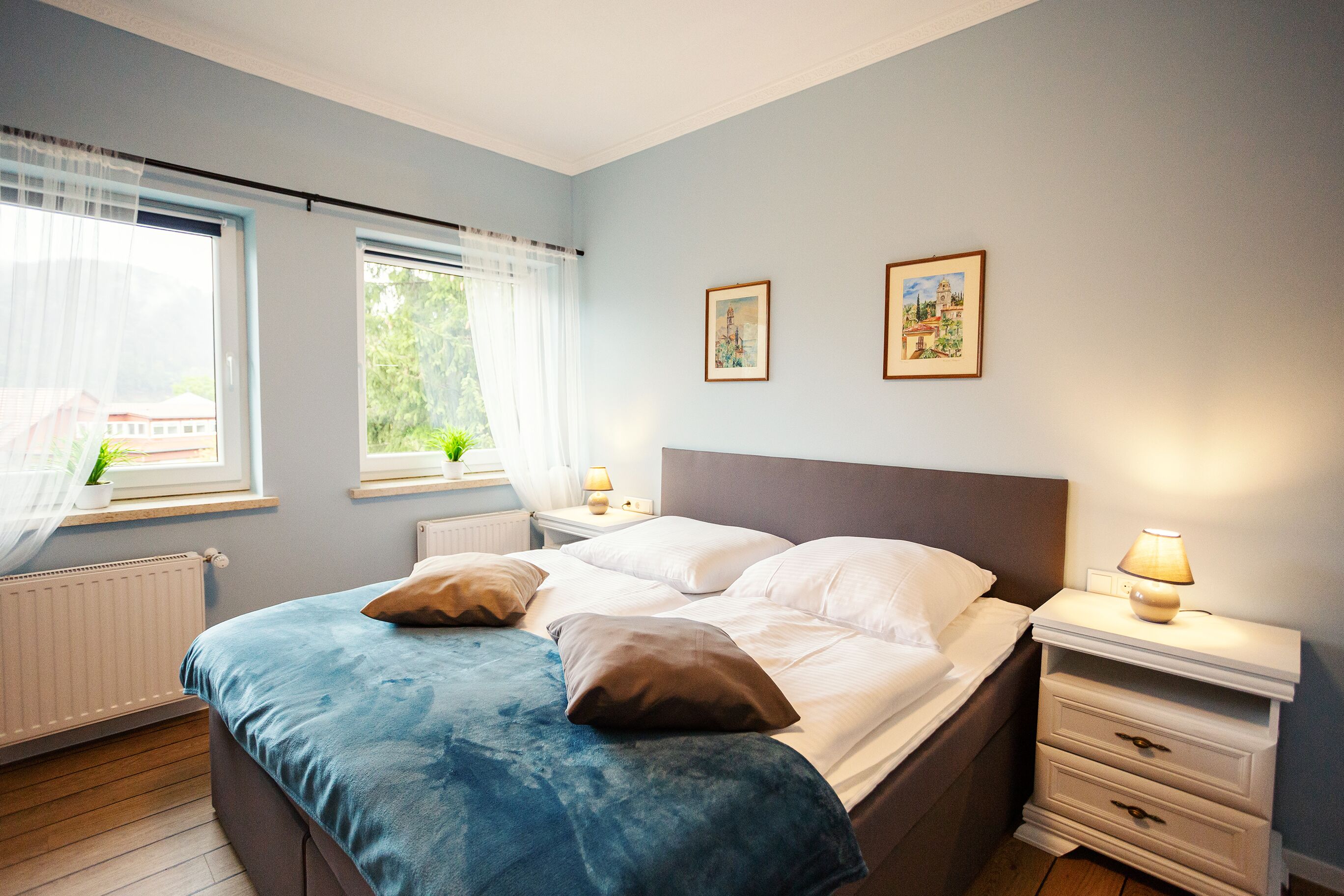 Un dormitorio con una cama, mesitas de noche y dos cuadros en la pared.