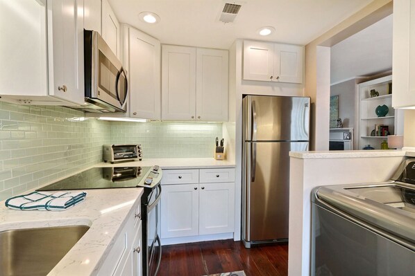 A modern kitchen with white cabinets, stainless steel appliances, and a tiled backsplash.