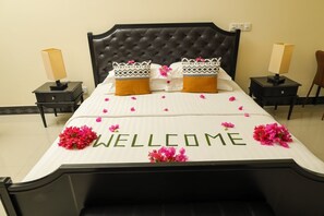 Una cama bien hecha con un cartel de 'WELCOME', dos almohadas y flores rosadas.