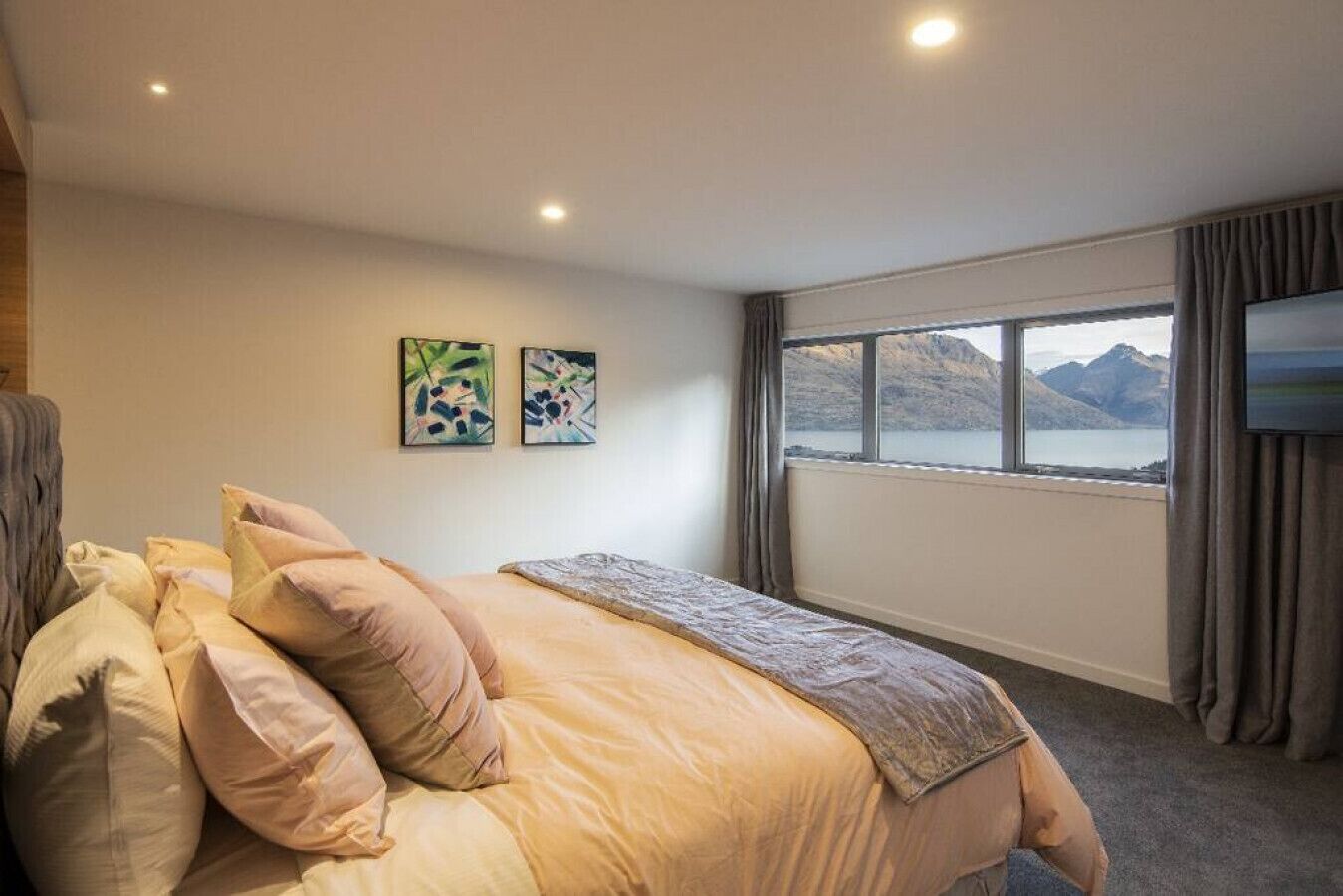 Une chambre à coucher avec un lit, des oreillers, une couverture, deux œuvres d’art murales, une télévision et une fenêtre donnant sur une vue sur les montagnes.