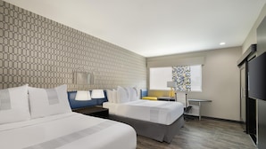 A hotel room with two beds, a desk, a chair, a TV, and a patterned wall.