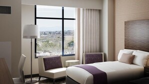 A modern hotel room with a large bed, a desk, a chair, and a view of a cityscape through large windows. - Estrella at Casino Del Sol (Tucson)
