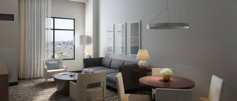 Une chambre d’hôtel avec un canapé, deux fauteuils, une petite table, une lampe et une vue sur la ville, visible à travers une grande fenêtre.