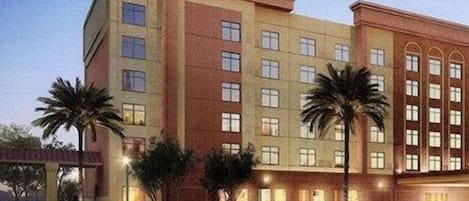 A multi-story hotel with a flat facade, large windows, and palm trees in front.