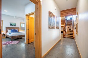 Une chambre d’hôtel moderne avec un escalier en bois, un lit avec des oreillers bleus et des œuvres d’art accrochées aux murs.