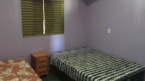 Een kleine slaapkamer met een enkel bed, een houten dressoir en een raam met luxaflex.