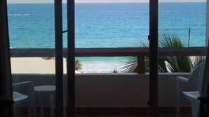 Un balcon avec vue sur l’océan, des chaises blanches et une petite table.