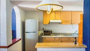 Une cuisine compacte avec des meubles en bois, un four à micro-ondes encastré et un réfrigérateur blanc.