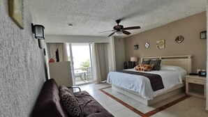 Une chambre d’hôtel avec un lit, un ventilateur de plafond, une table de chevet, un bureau et une vue sur l’extérieur.