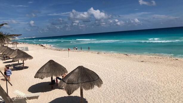 Une plage avec des parasols en chaume et une vue dégagée sur l’océan.