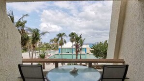 Un balcon avec une table ronde et deux chaises, donnant sur une piscine et des palmiers.